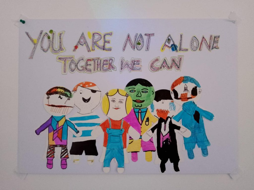 An art poster made by one of our clients. It reads "You are not alone - together we can." There is cut and glued artwork of 6 people.